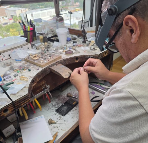 A jeweler's hands working on a gold piece at a workbench.